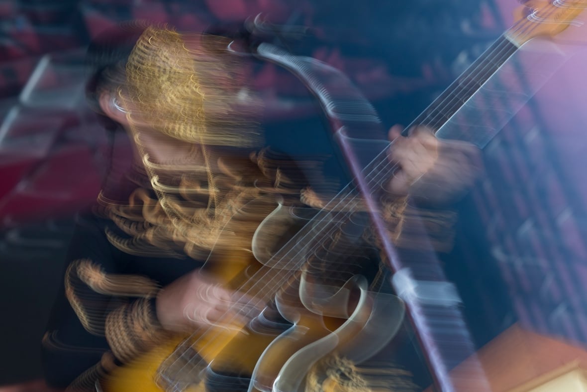 A person playing guitar wearing a decorative gold face mask, and he's blurred to show motion.