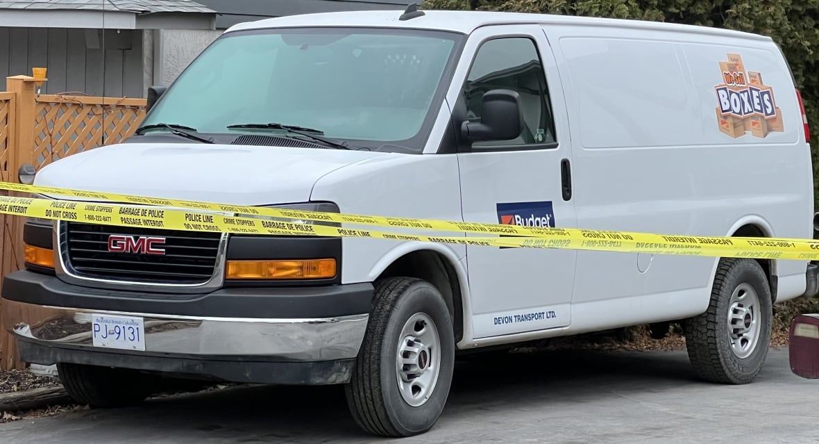A white budget cargo van is parked on the side of a street, and blocked off with police tape.
