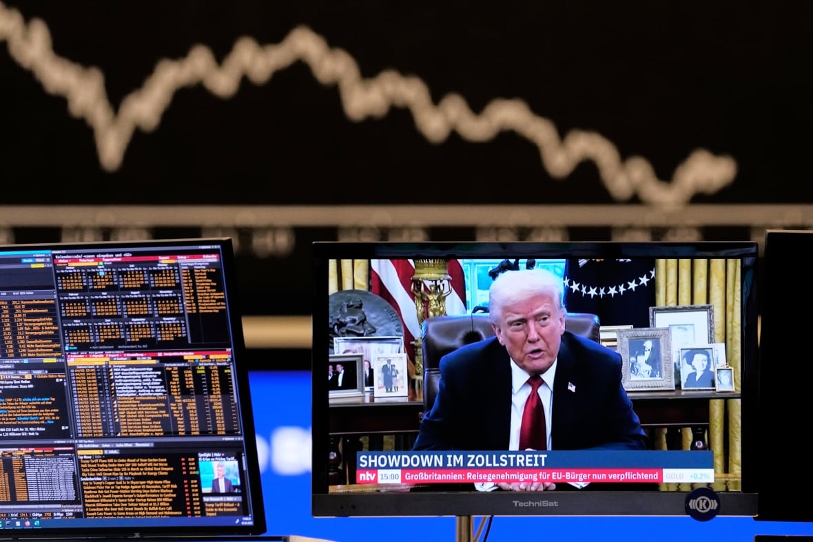 A TV monitor shows a person speaking at a desk as other monitors show financial data.