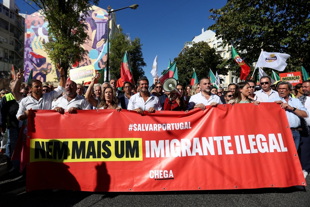 A group of people march in the streets holding a red banner containing anti-immigration slogans