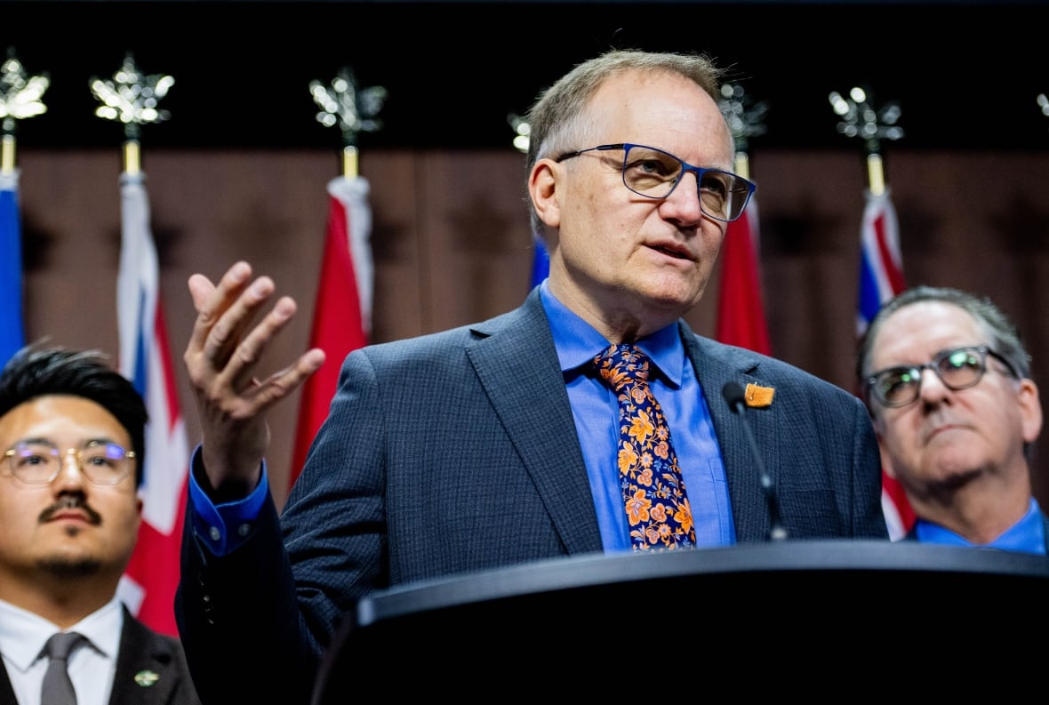 A man with thin grey hair speaks at a podium.