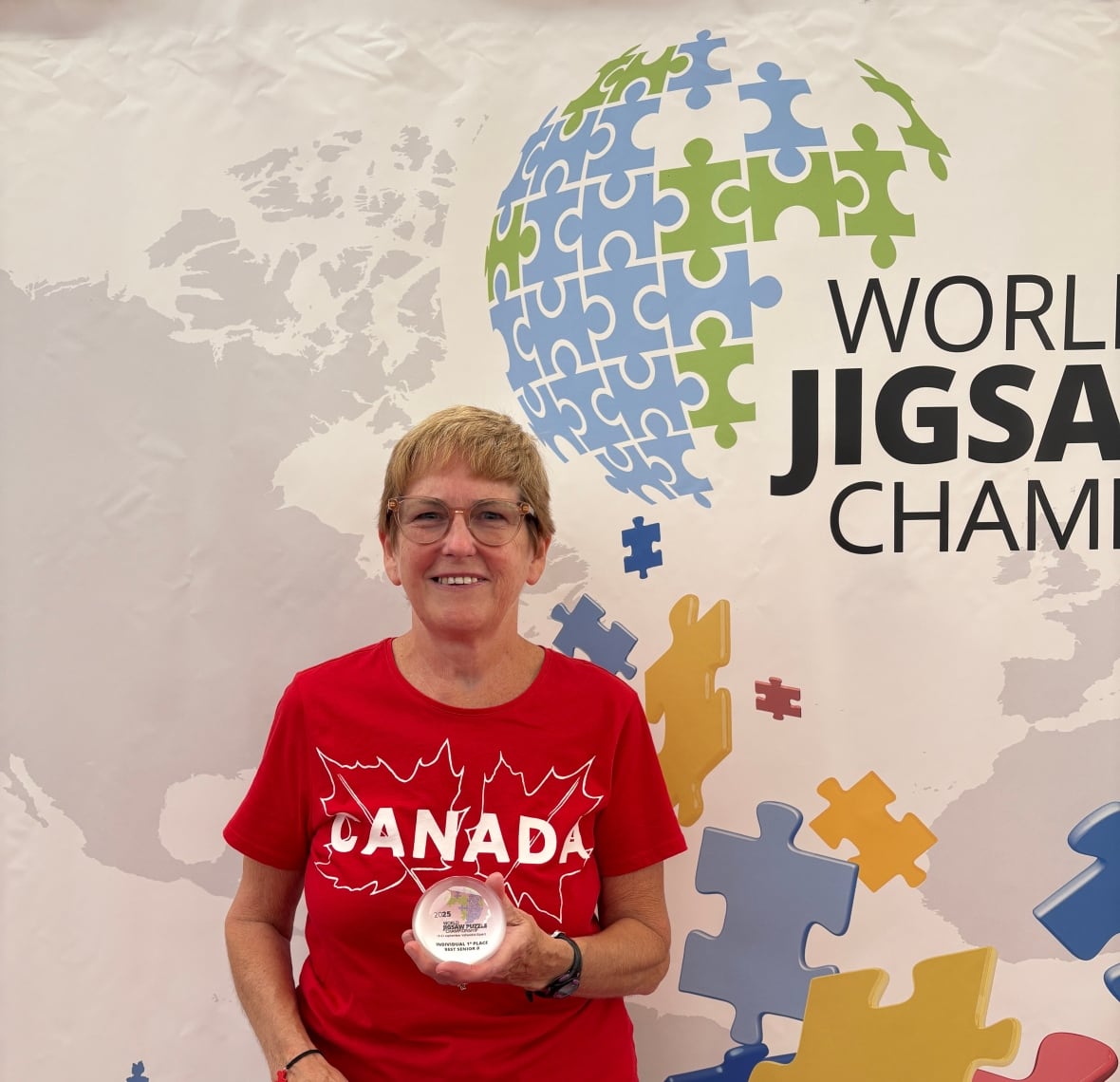 Woman stands in front of championship backdrop holding trophy and wearing Canada shirt