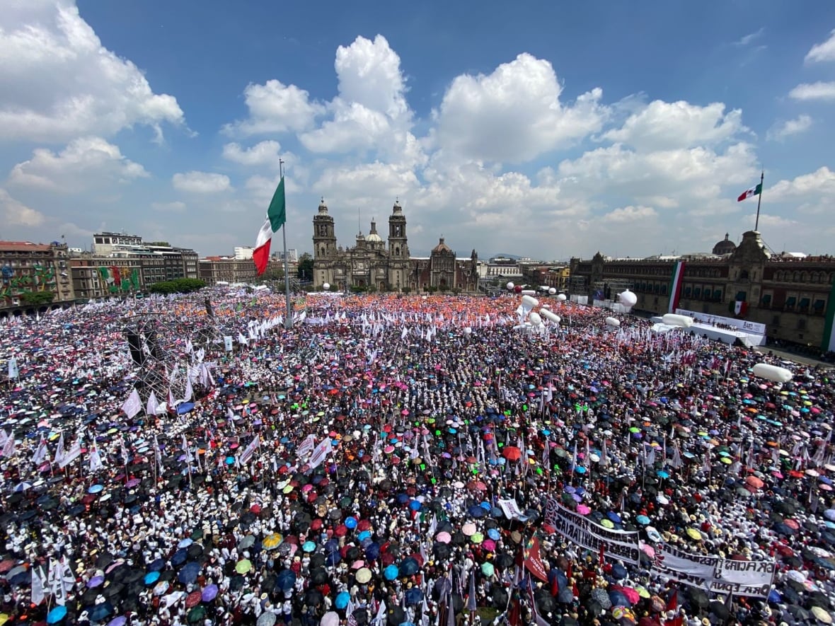 A birds eye view of a multiude of people, with white flags and balloons in the air, crowded into a central square.