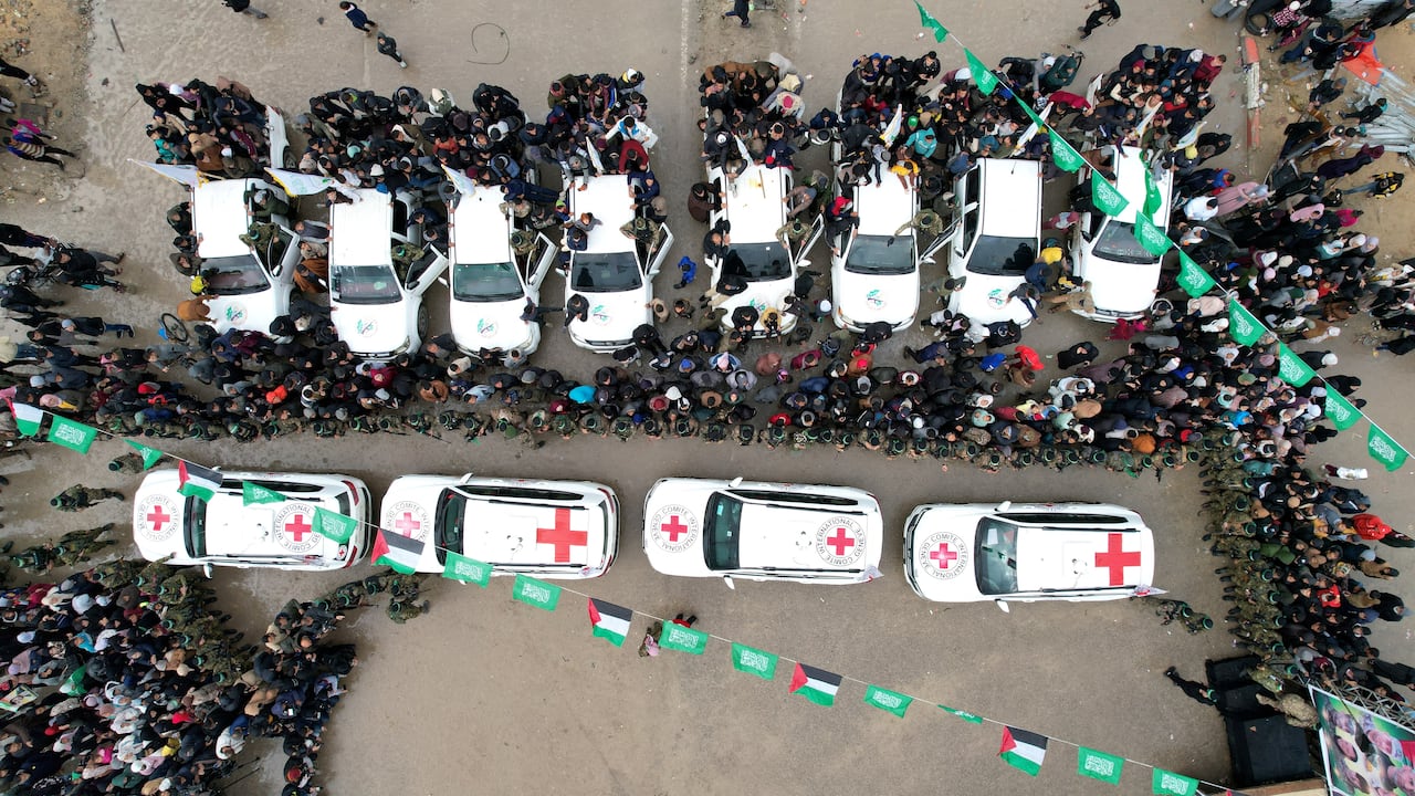 A photo taken from above shows a line of white vehicles with red crosses on them driving through a crowd
