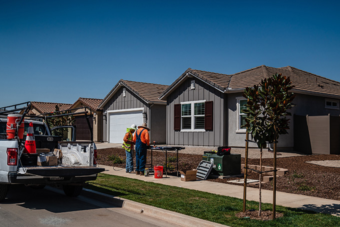 Two construction workers standing in front of homes in the Dixon Trails subdivision in Escondido, Calif., with fire-resistant features such as metal fences and tempered glass windows.