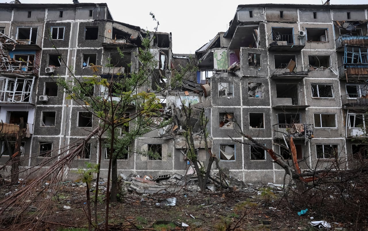 A damaged apartment building, with windows blown out, a section of the roof collapsed and trees felled, is shown.