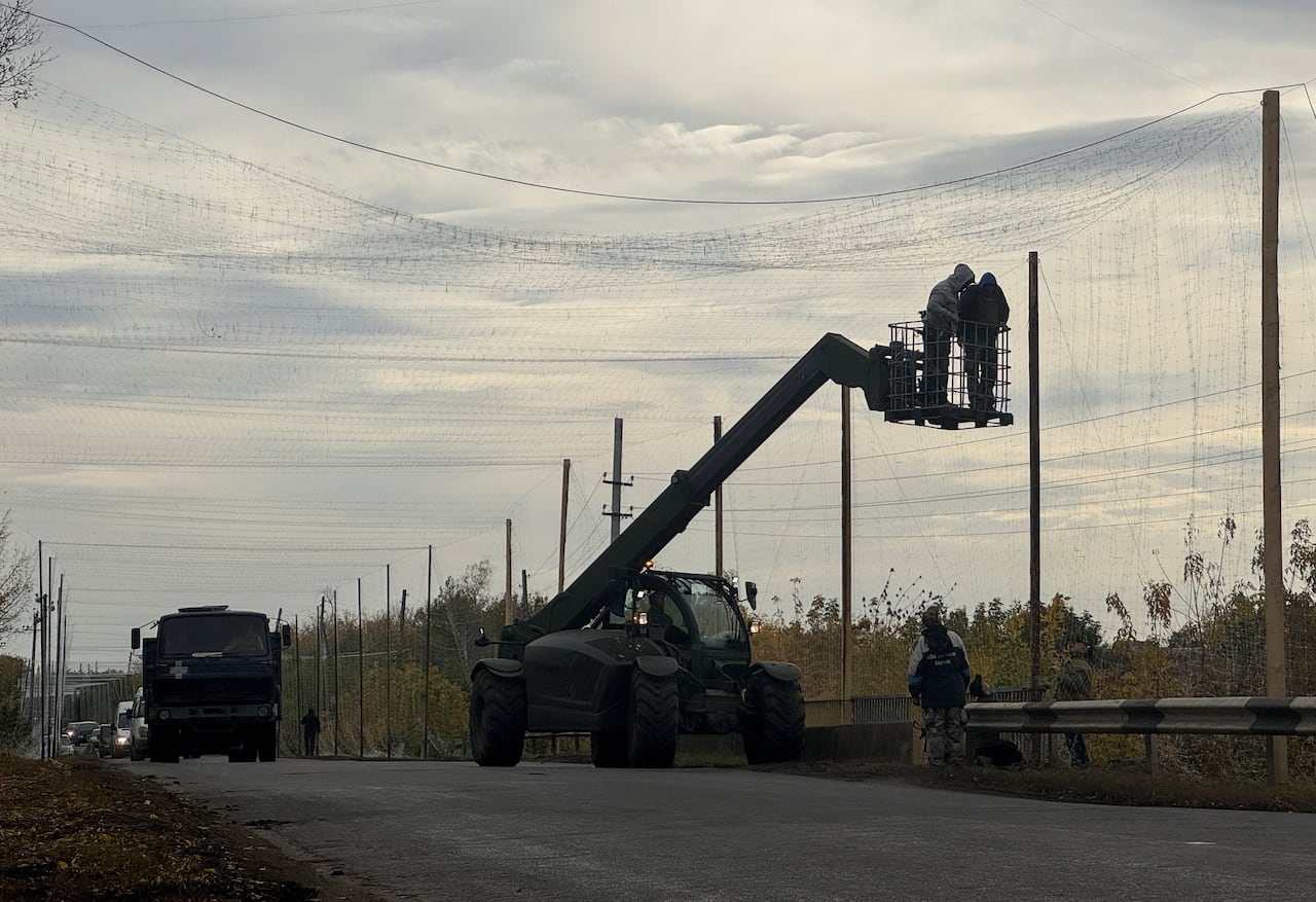 A lift truck is shown holding two men as mesh netting is installed above a road.