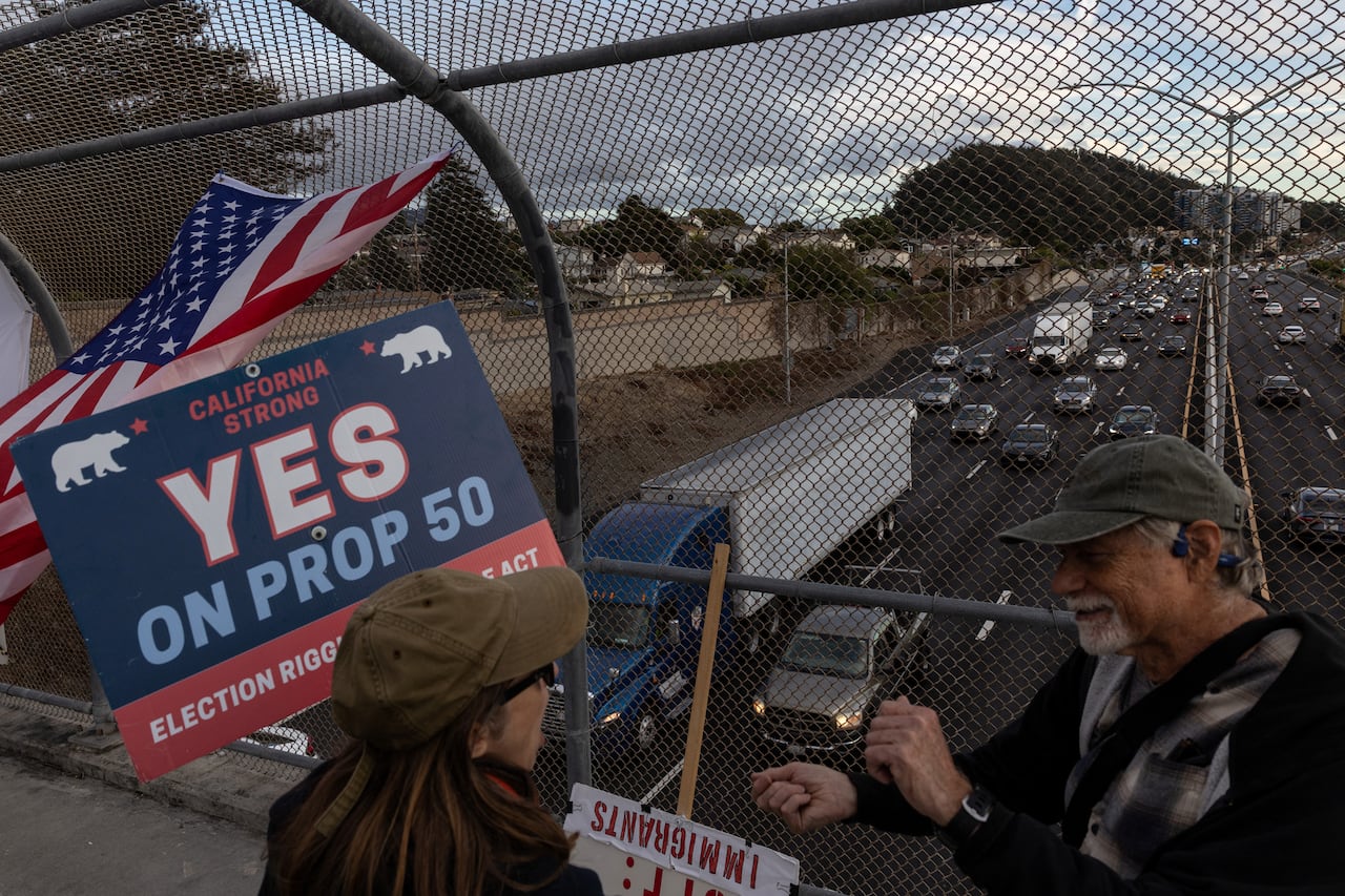 Two people, one holding a picket sign, stand on a highway overpass