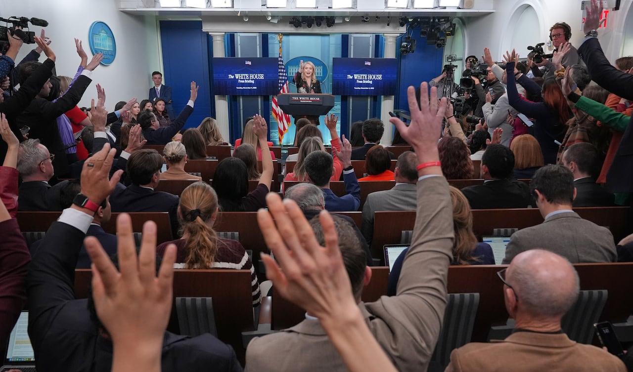 Reporters are seen raising their hands at a news conference.