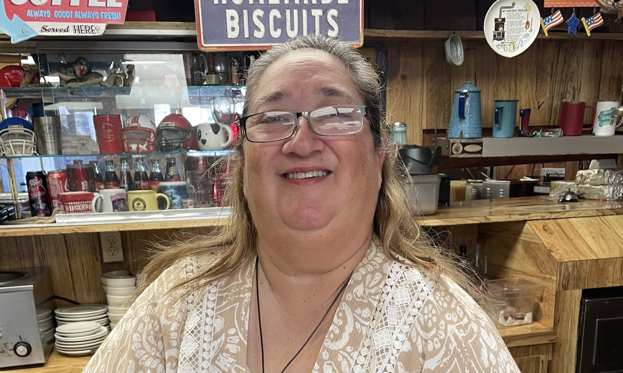 A woman stands smiling at a restaurant counter.