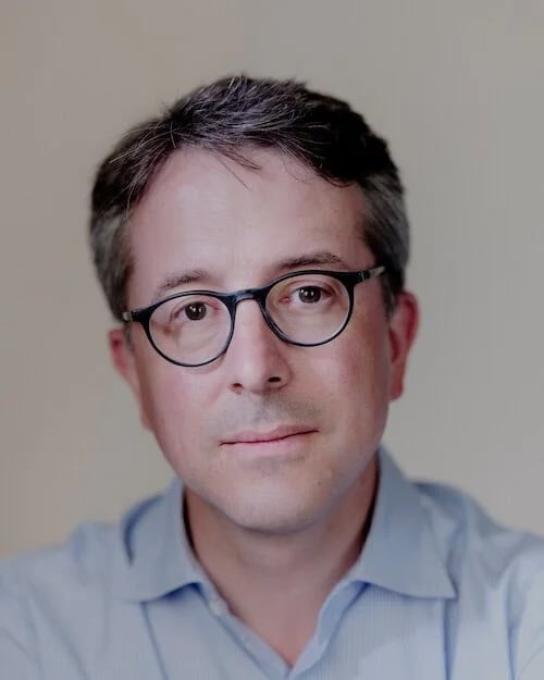 A man with glasses and short hair looks at the camera