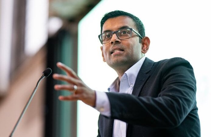 A man lectures at a podium while gesturing