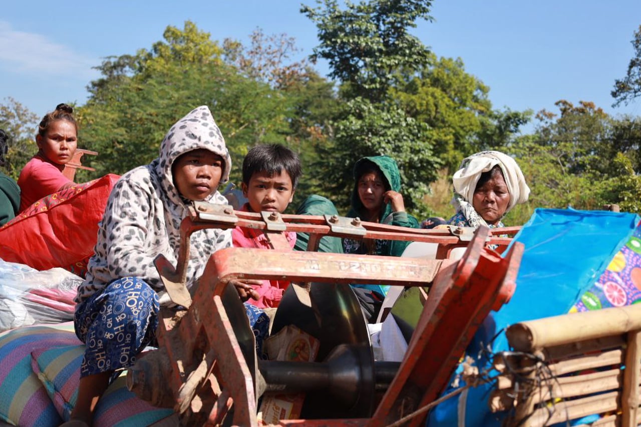 A group of people, including an older woman and young child, sit atop a moving tractor.