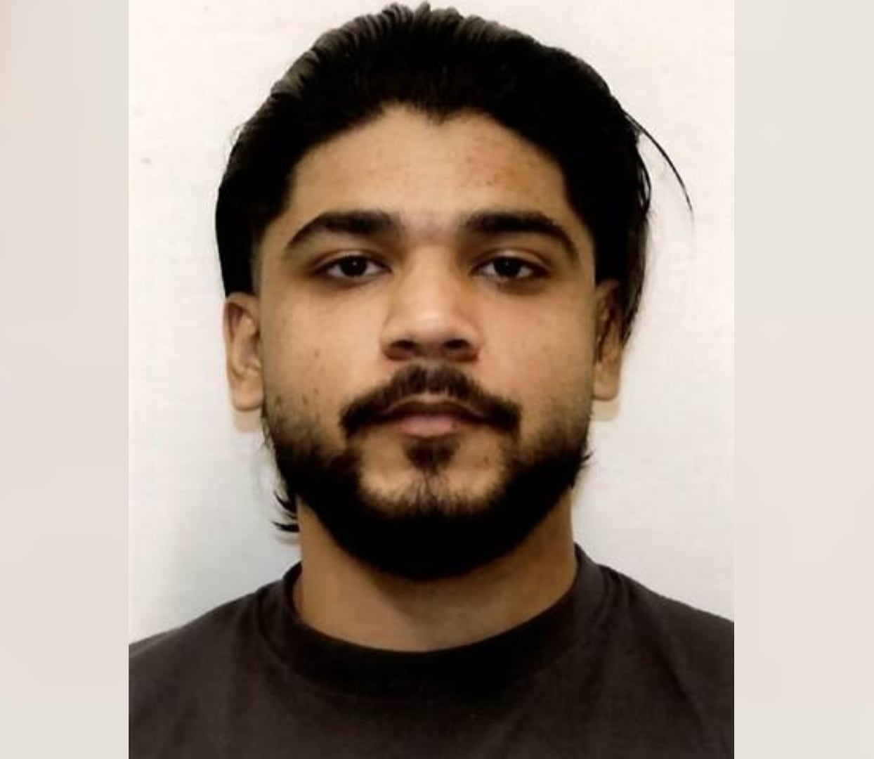 A South Asian man with a beard is seen in a mugshot.