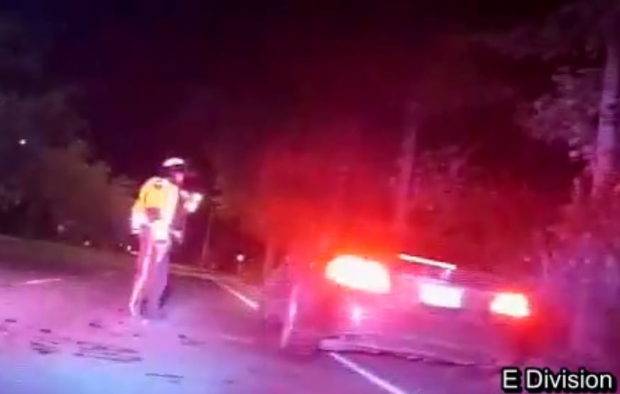An RCMP officer stands with his weapon drawn at a vehicle, in grainy nighttime footage.