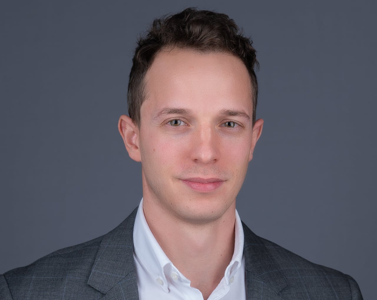 Portrait photo of an adult caucasian male wearing a grey suit jacket and white shirt with slightly open collar.