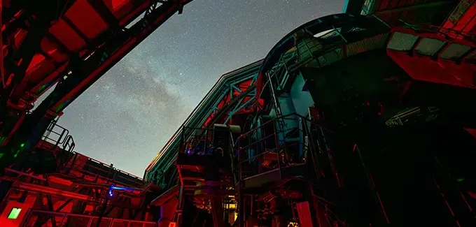 The night sky is seen from the vantage point of being inside an observatory with its dome open.