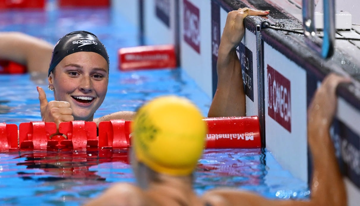 A women's swimmer gives a thumbs up in the pool.