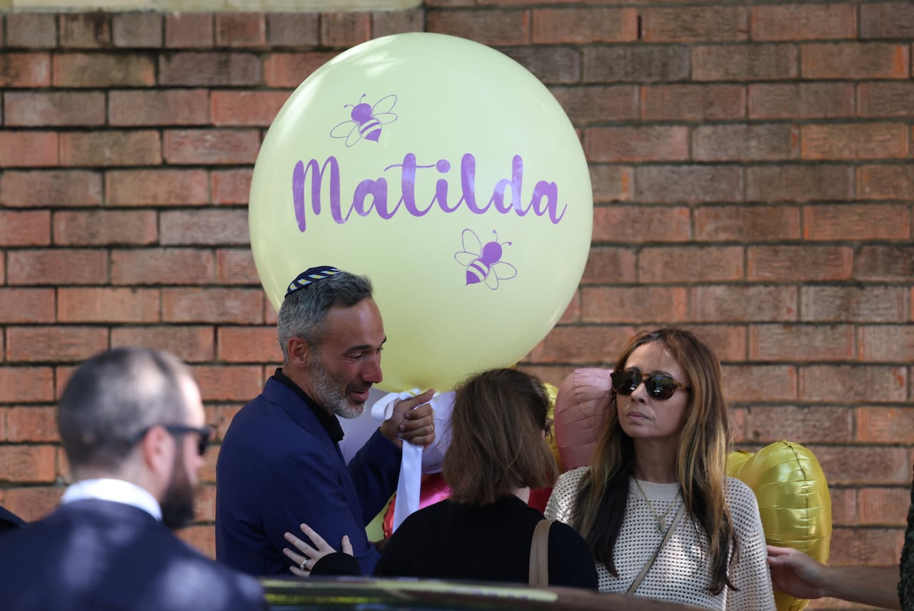 People stand close to each other, one holding a yellow balloon with the name Matilda on it