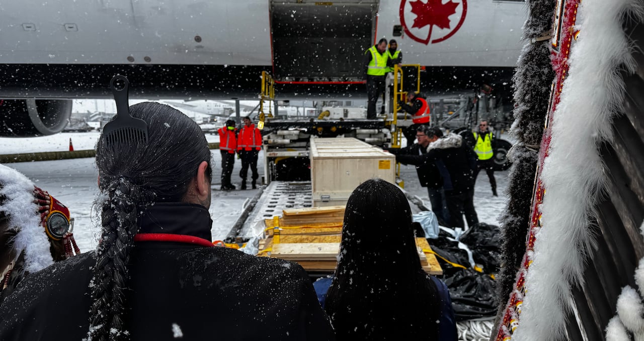 People watch as a large box is unloaded from a plane by workers.