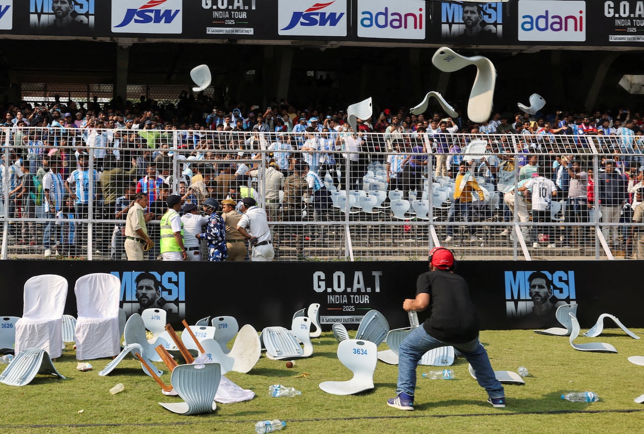 Broken chairs tossed around soccer field, with a man ducking from others being thrown
